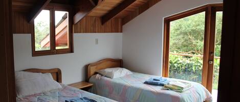 A bedroom with two beds, wooden beams on the ceiling, and a large window.