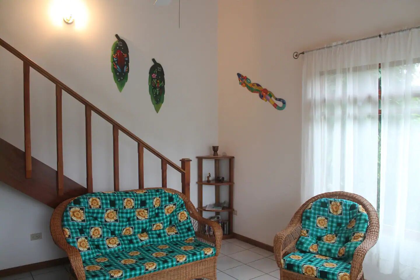 A living room with two wicker chairs, a wooden staircase, and a shelf with decorative items.