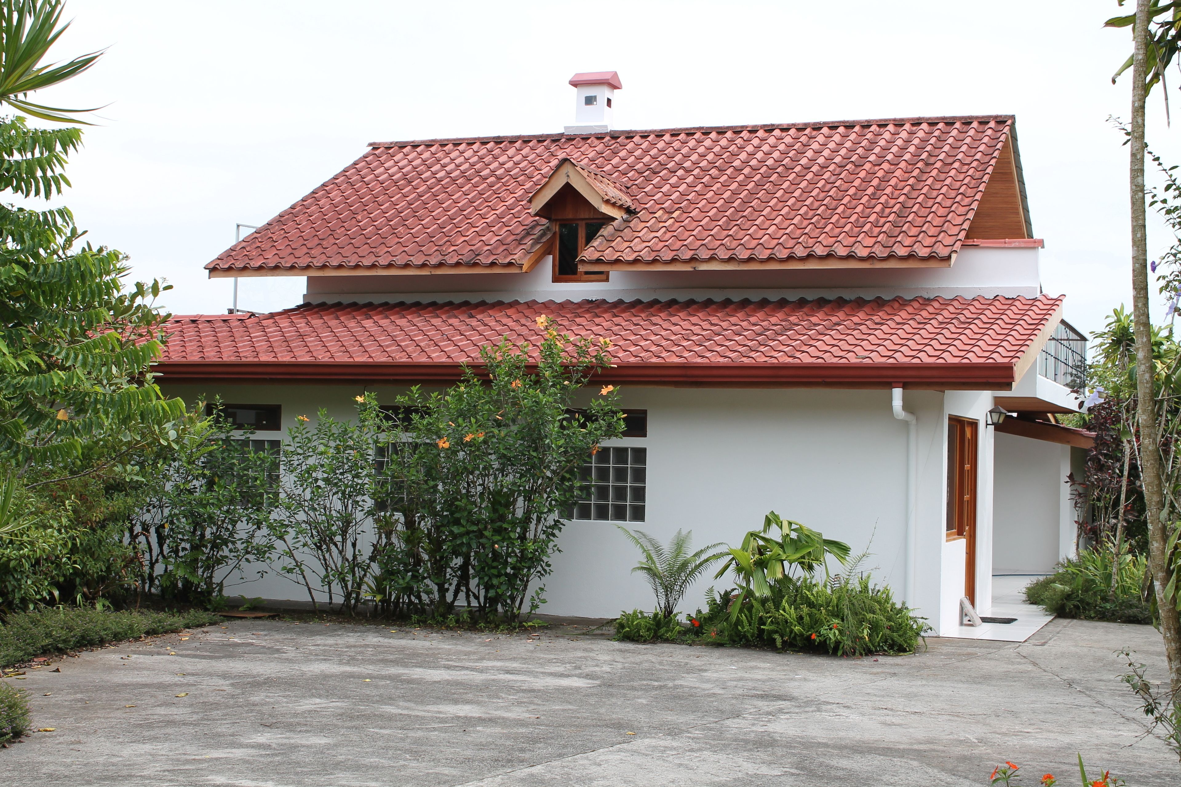 A two-story house with a red-tiled roof, white walls, and a small porch.