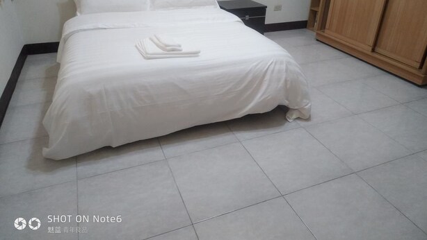A neatly made bed with white bedding in a room with tiled flooring and wooden furniture. - Autumn Water (Jinning)