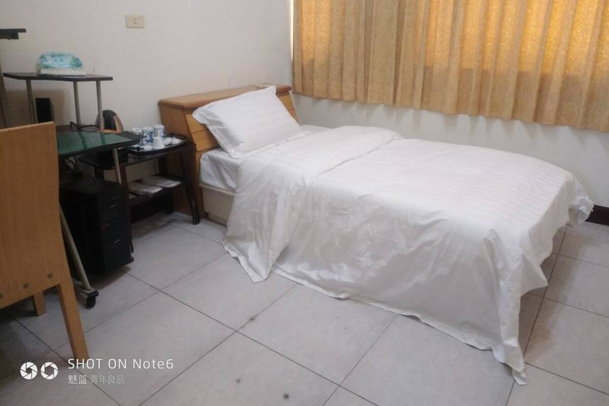 Quarto com uma cama de solteiro, escrivaninha com cadeira e janela com cortinas.