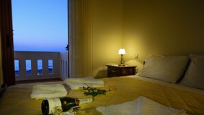 A hotel room with a bed, a nightstand with a lamp, and a view of the sea through the window.
