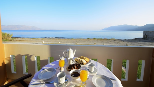 A table set for breakfast with a view of a calm sea and distant mountains.