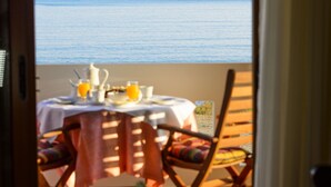 An open door leading to a balcony with a table set for breakfast, overlooking the sea.