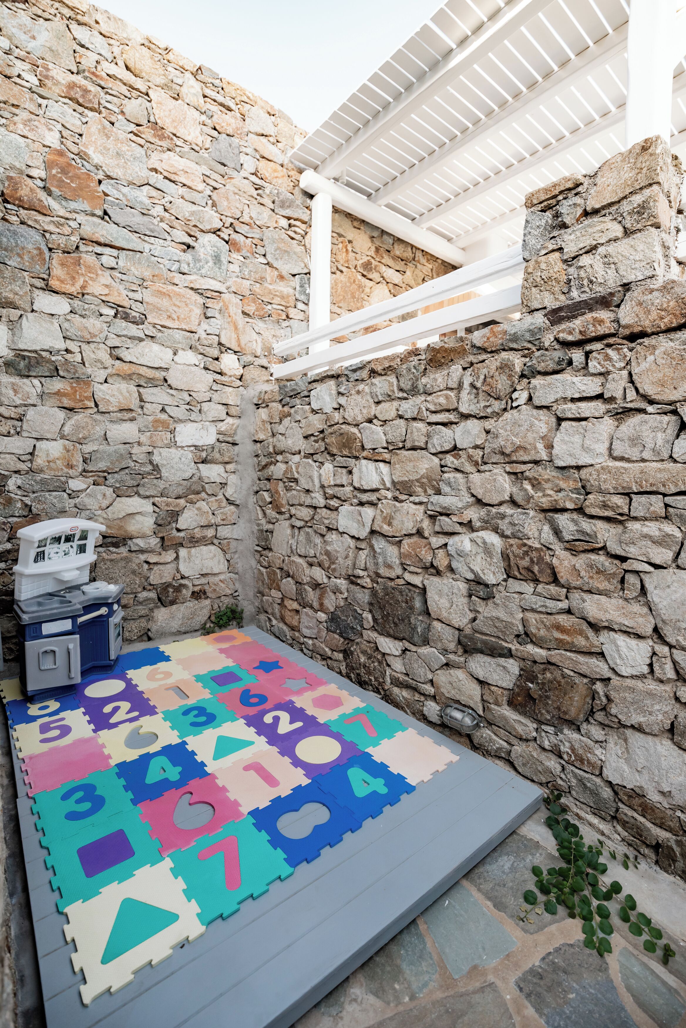 A stone-walled room with a colorful play mat and a white ceiling structure.