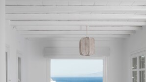 Una habitación blanca con un ventanal grande que da al océano, un sofá blanco, una mesita y una silla a rayas.