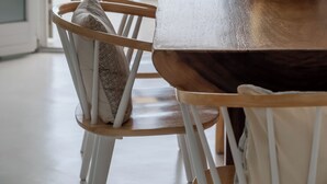 Comedor con mesa de madera y sillas blancas, con vista al mar.