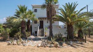 Una casa a due piani con una scalinata in pietra che conduce all'ingresso, circondata da palme e cactus.