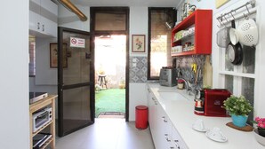 Uma cozinha com geladeira, forno e uma lixeira vermelha. Há uma janela com vista para um jardim.