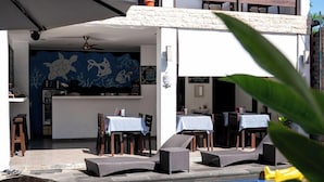 Ein moderner Poolbereich im Freien mit Liegestühlen und Tischen, ein Essbereich mit blau-weiß kariertem Tischläufer und ein Wandgemälde mit Meereslebewesen.