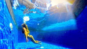 Eine Person schwimmt in einem Pool mit klarem, blauem Wasser und einem gefliesten Boden.
