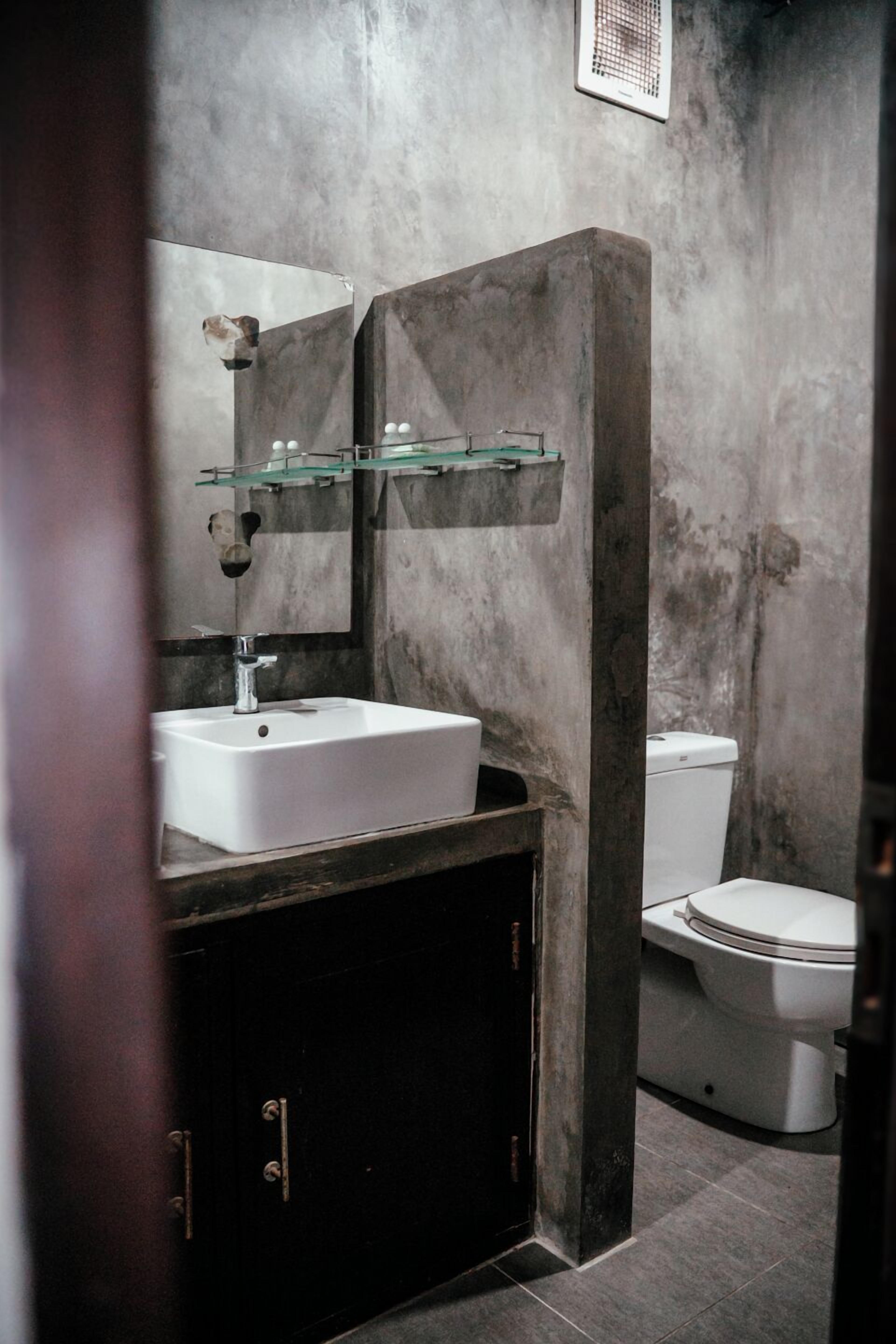 A bathroom with a white sink, a glass shelf, a dark cabinet, and a white toilet.