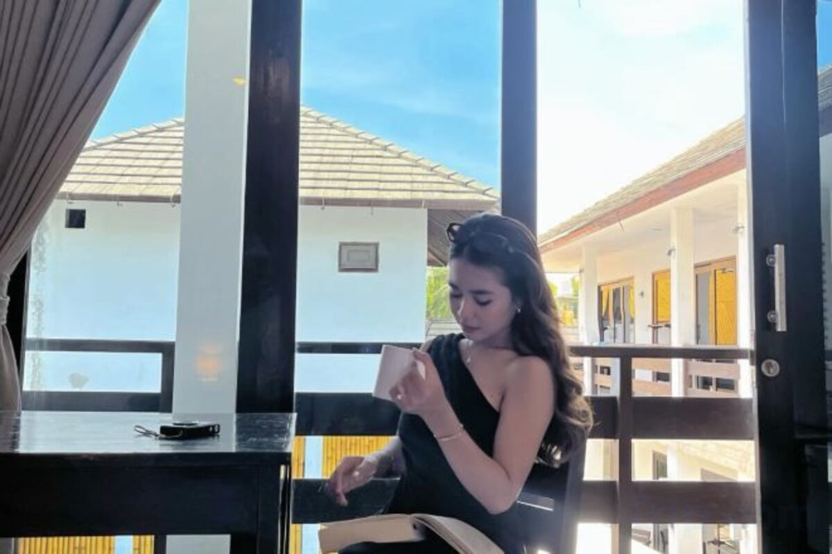 A person seated at a table with a window view of a building with a tiled roof.