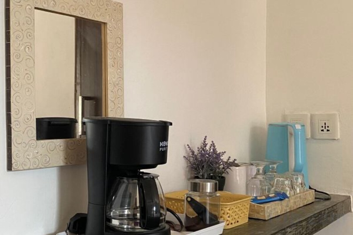 A coffee station with a coffee maker, a mirror, and a water dispenser on a countertop.