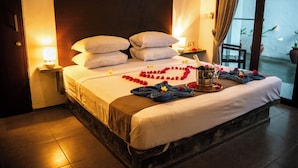 Ein ordentlich bezogenes Bett mit einer blumigen Herz-Arrangement, einer Champagnerflasche und Handtüchern in einem Hotelzimmer.