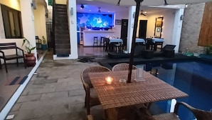Ein Essbereich im Freien mit Pool, Korbmöbeln und einer Bar im Hintergrund.