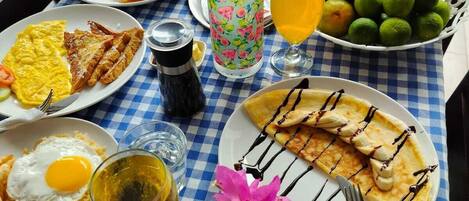 A table set with breakfast items including eggs, toast, and fruit, with a checkered tablecloth and a view of a pool.