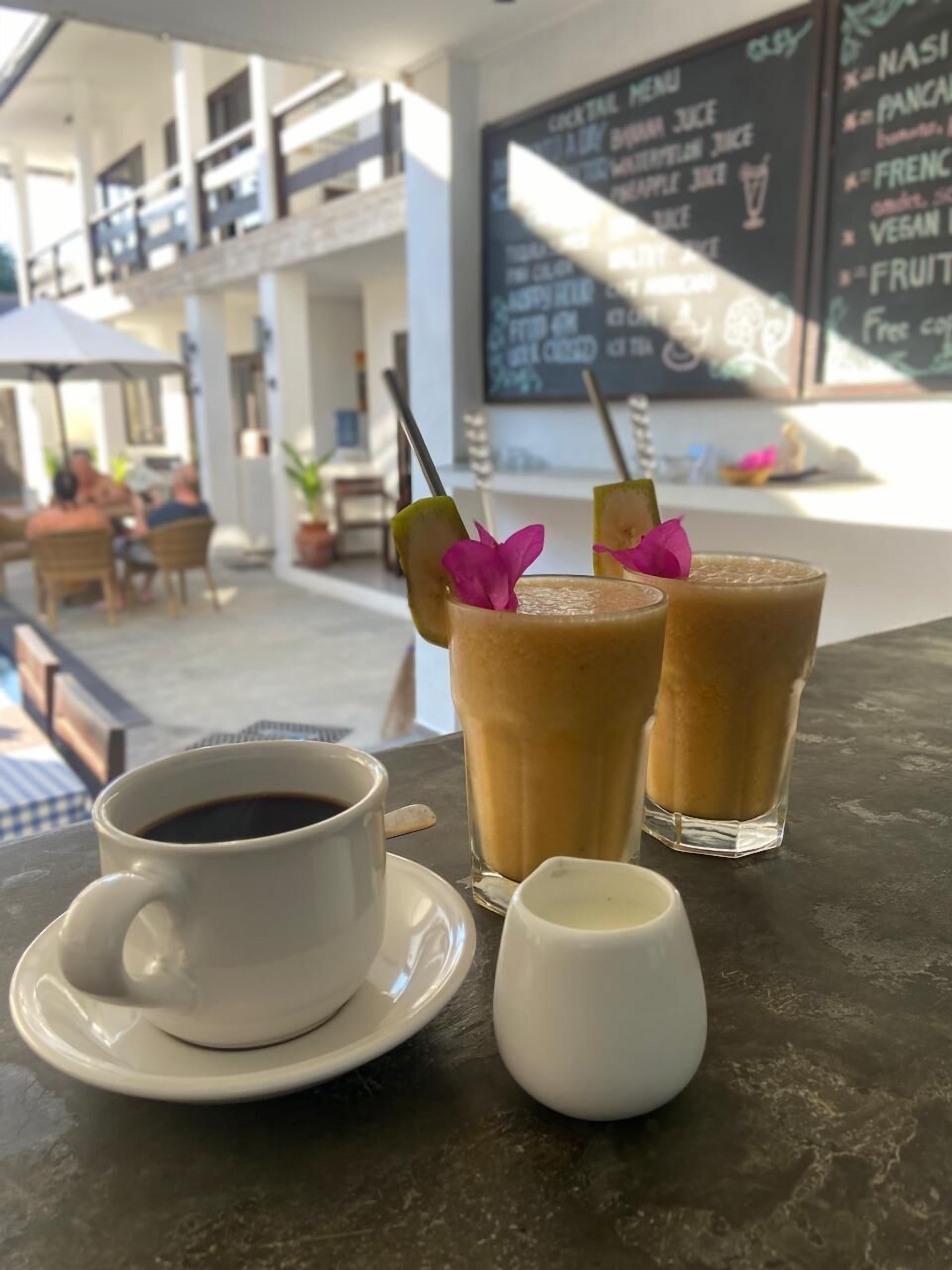 A table with a cup of coffee, two iced drinks with garnishes, and a menu board in the background.