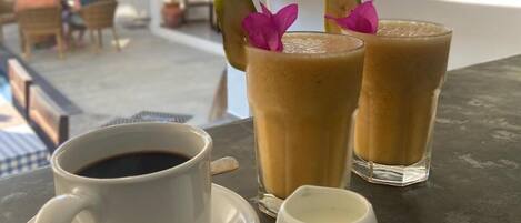 A table with a cup of coffee, two iced drinks with garnishes, and a menu board in the background.