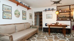 A cozy living room with a stone floor, a wooden sofa, a dining table, and various decorative items.