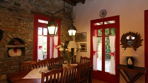 Un comedor con pared de piedra, muebles de madera y ventanas con marcos rojos.