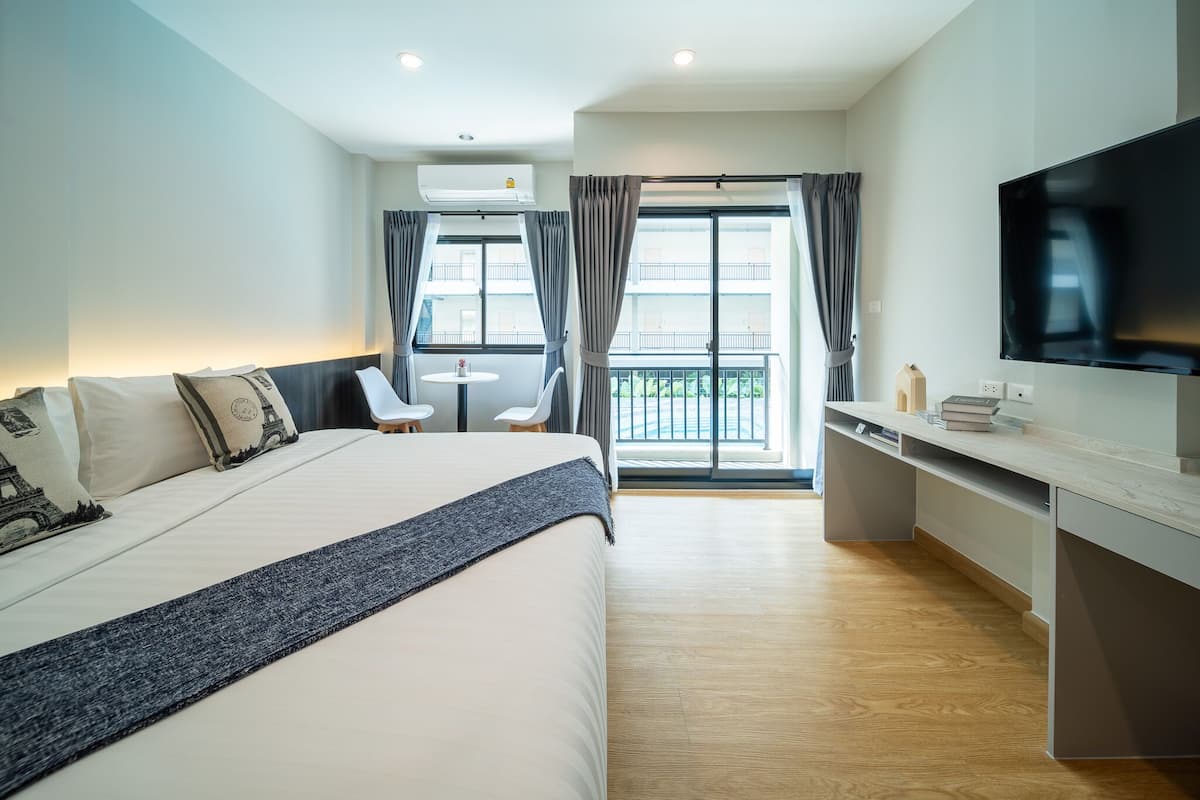 A hotel room with a bed, a desk, a TV, and a balcony with curtains.