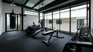 A gym with exercise equipment, a punching bag, and large windows. - College Haus (Bangkok)