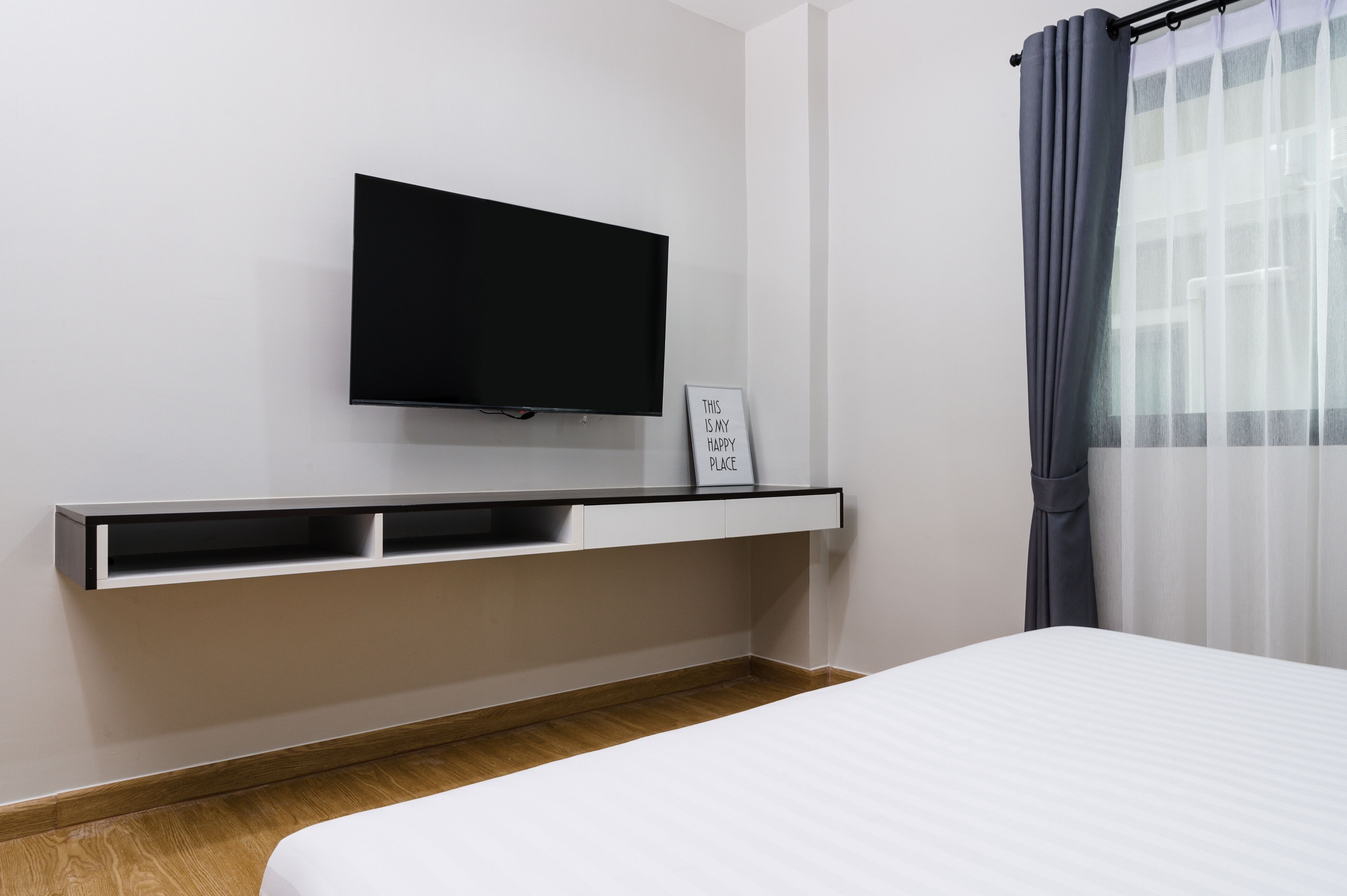 Een moderne hotelkamer met een tv, een nachtkastje met een bordje en een raam met gordijnen.