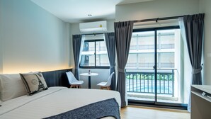 A hotel room with a bed, a small table with two chairs, a balcony with a view, and an air conditioning unit. - College Haus (Bangkok)