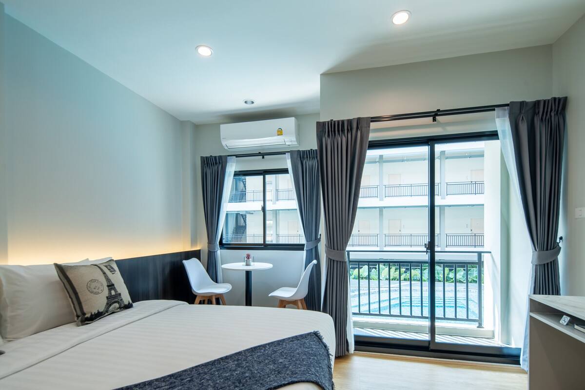 A hotel room with a bed, a small table with two chairs, a balcony with a view, and an air conditioning unit.