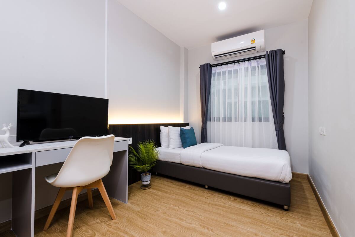 A modern room with a bed, a desk with a computer, and an air conditioning unit.
