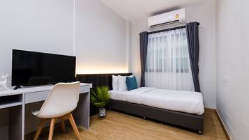 Quarto moderno com cama, escrivaninha com computador e aparelho de ar condicionado.