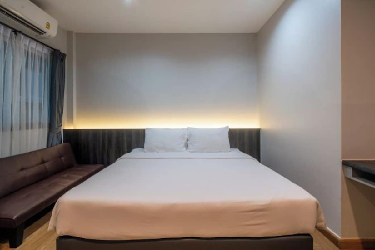 A hotel room with a bed, a bench, and a headboard with a light.
