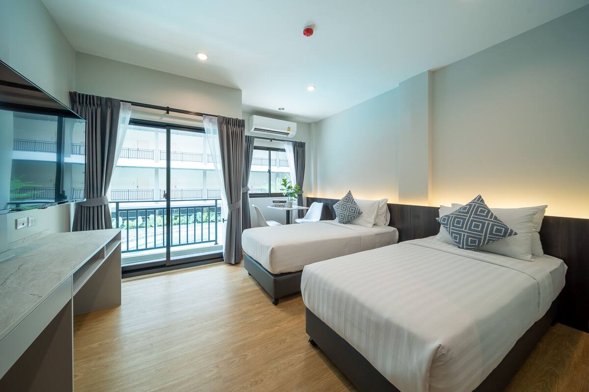A modern hotel room with two beds, a desk, and a balcony with a view.
