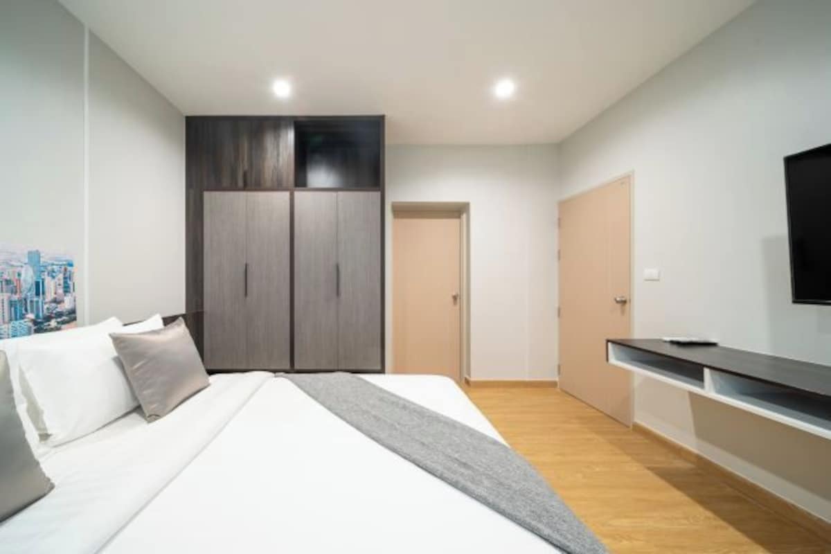 A bedroom with a bed, wardrobe, TV, and a cityscape painting.