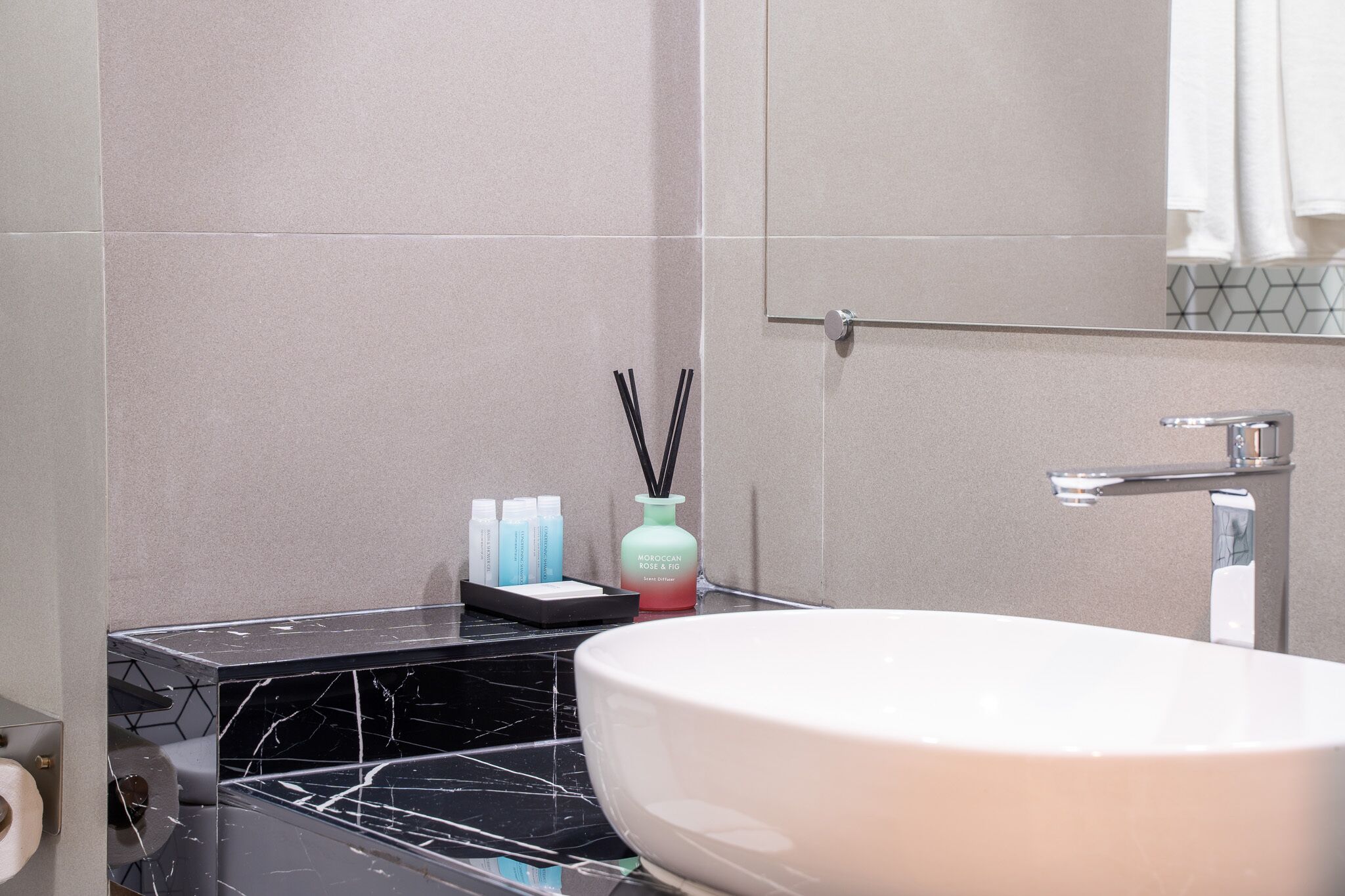 Un baño con un lavabo blanco, un espejo y un perchero para toallas. Hay artículos de aseo en la encimera.