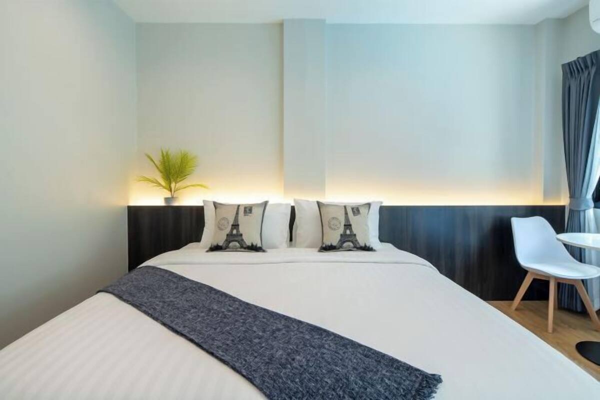 A hotel room with a bed, a desk, a chair, and a potted plant.