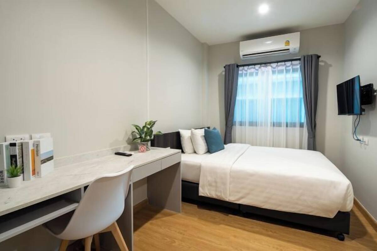A hotel room with a bed, desk, chair, air conditioning unit, and a television.