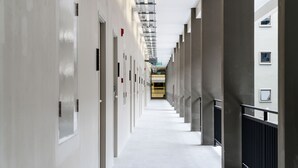 A long, narrow hallway with doors on both sides, leading to a bright room at the end. - College Haus (Bangkok)