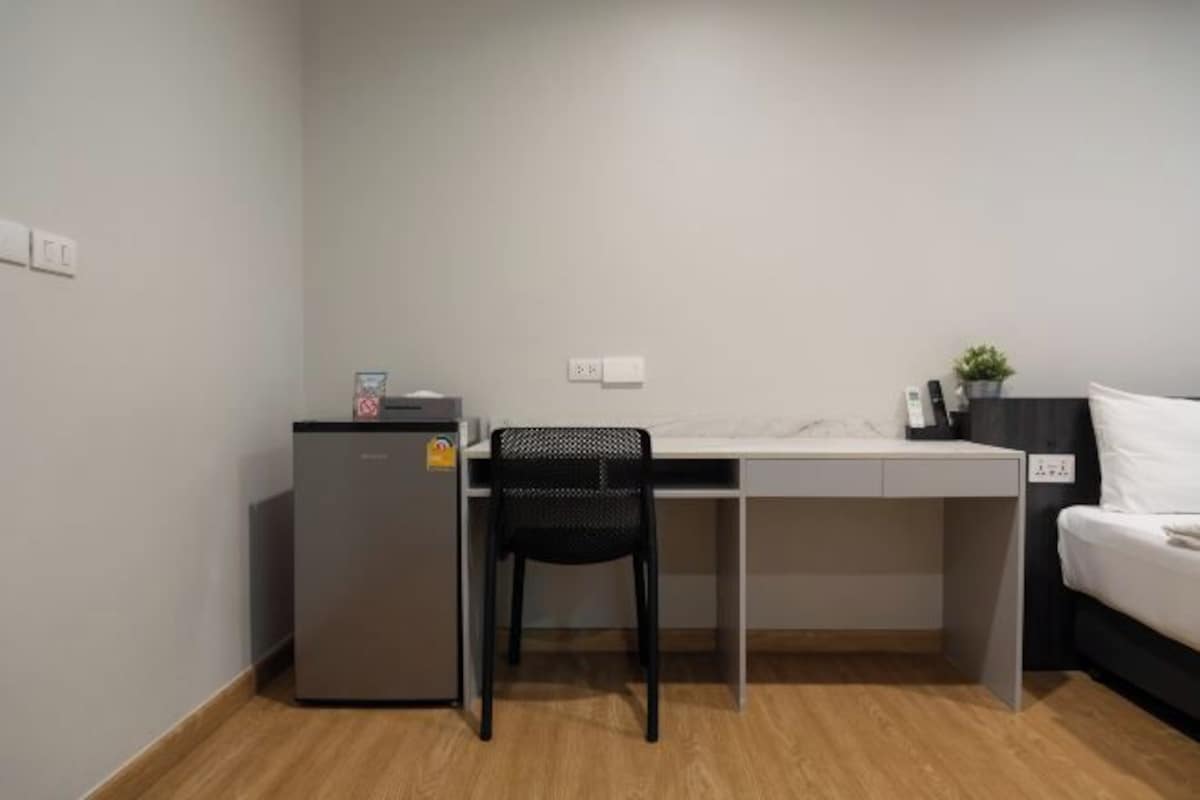 A compact room with a small kitchenette, a desk, a chair, and a bed.
