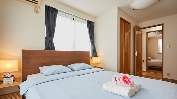A hotel room with a large bed, two bedside tables, a nightstand, a window with curtains, and a door leading to another room. - Senior villa 4BR, Shinjuku Okubo (東京)