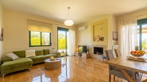 A spacious living room with a green sofa, a wooden dining table, and a fireplace. - Holiday villa with private pool (Ξηροκάμπι)