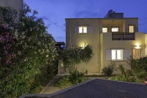 Un bâtiment à deux étages doté d’un balcon et d’un petit jardin agrémenté de plantes à fleurs.