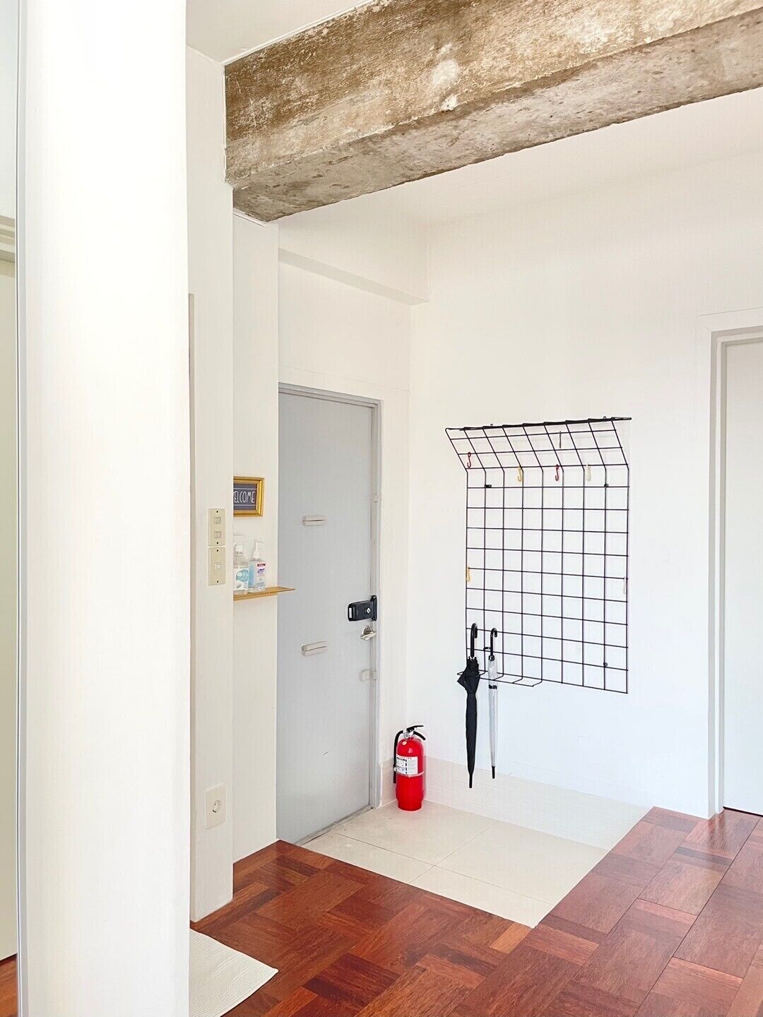A hallway with a wooden floor, a fire extinguisher, and a metal grid wall decoration.