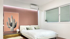Ein modernes Schlafzimmer mit einem Bett, einer Kaktus-Kunstwerk, einem Fenster mit Jalousien und einer Deckenleuchte.