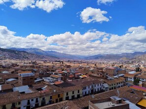 A densely packed urban area with a mix of traditional and modern buildings, under a clear sky with scattered clouds. - El Balcón del Sol (Cusco)