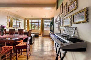 A dining area with a piano, wooden chairs, a table with a tablecloth, and framed pictures on the wall. - El Balcón del Sol (Cusco)