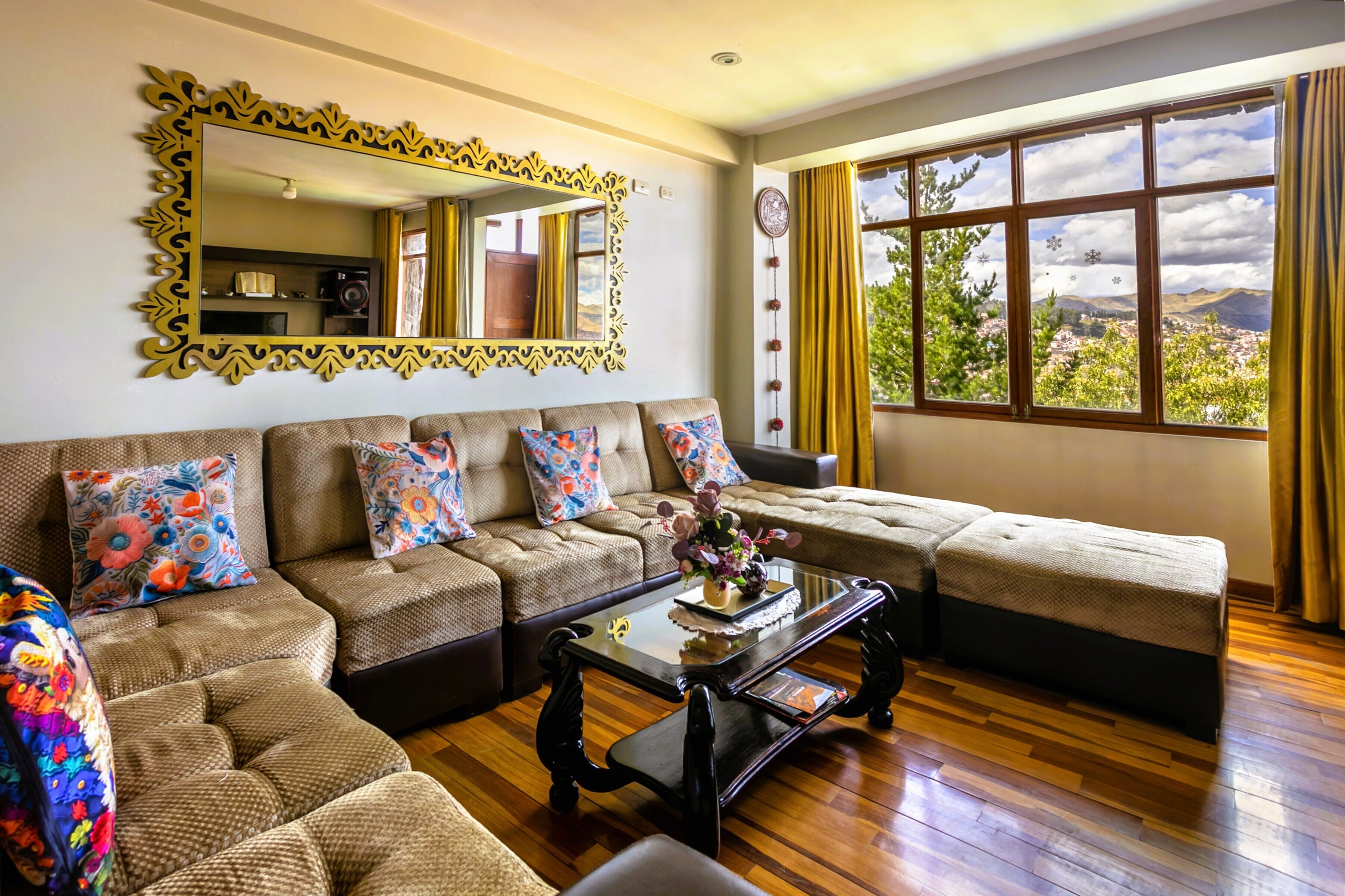 A living room with a sofa set, a coffee table, a large mirror, and a window with a view of greenery.