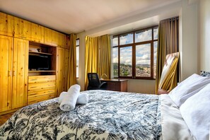 A hotel room with a bed, a desk, a chair, a television, and a window with curtains. - El Balcón del Sol (Cusco)