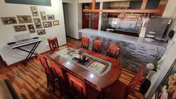 A dining area with a wooden table and chairs, a piano, and framed photos on the wall.